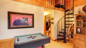 A cozy room with a pool table, wooden walls, a spiral staircase, and a framed picture on the wall.