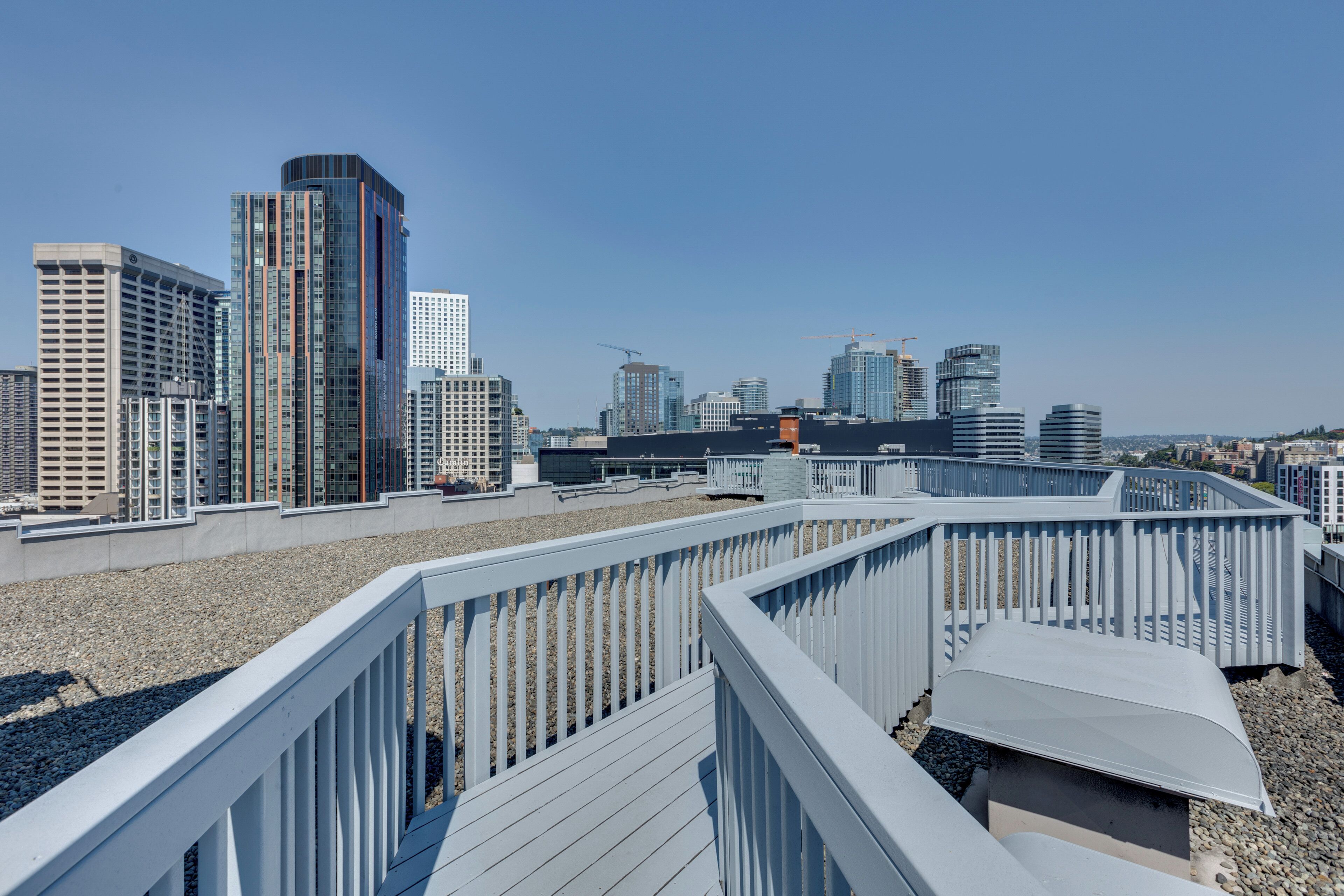 Una terraza en la azotea con vistas al horizonte de una ciudad, con edificios modernos y un cielo despejado.