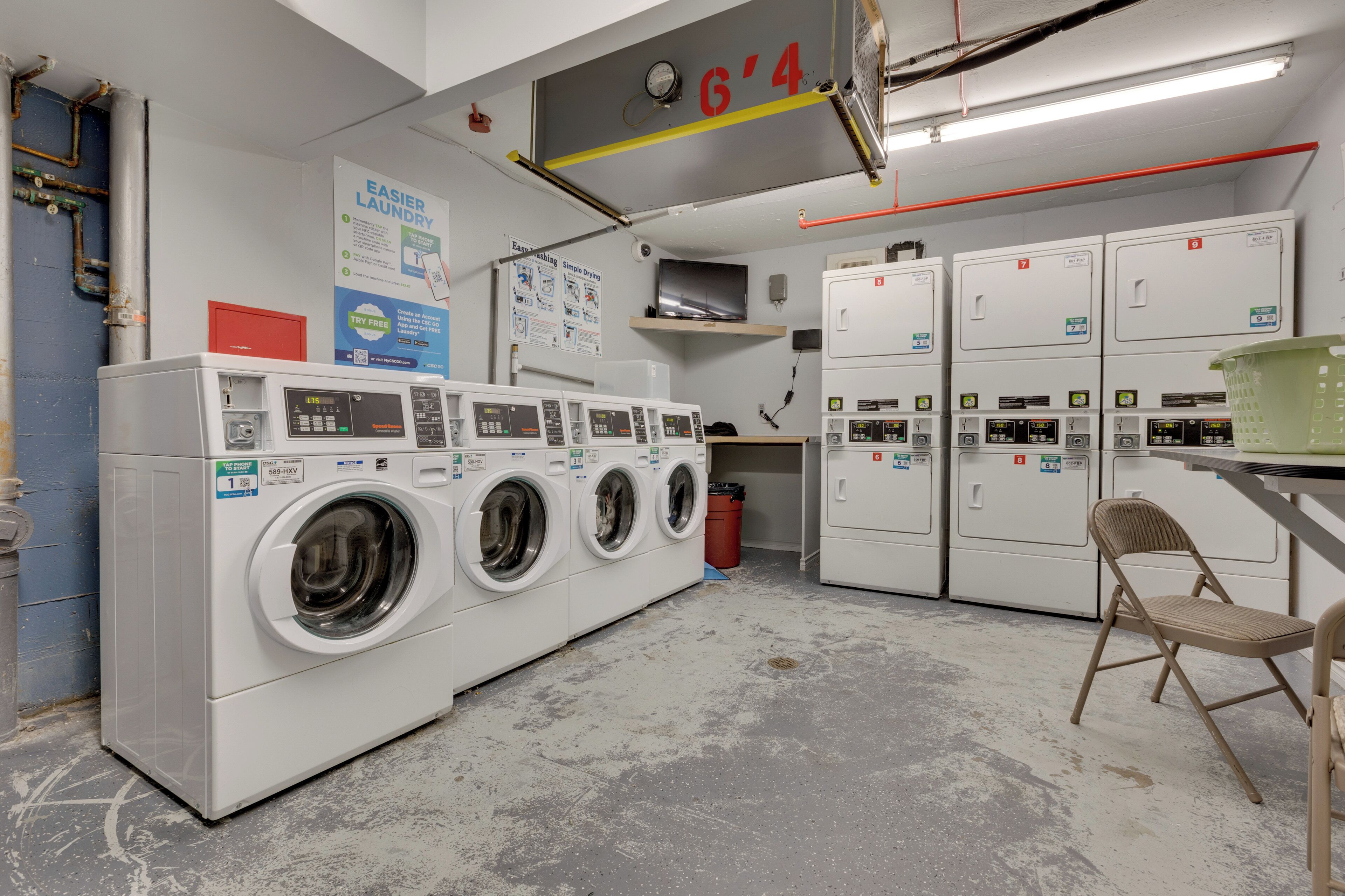 Une buanderie équipée de plusieurs machines à laver, d’un extincteur et d’un panneau indiquant le numéro de l’étage.