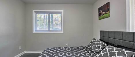 A bedroom with a bed, a window, and a painting on the wall.