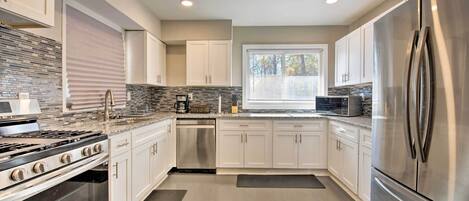 A modern kitchen with stainless steel appliances, white cabinets, and a tiled backsplash.
