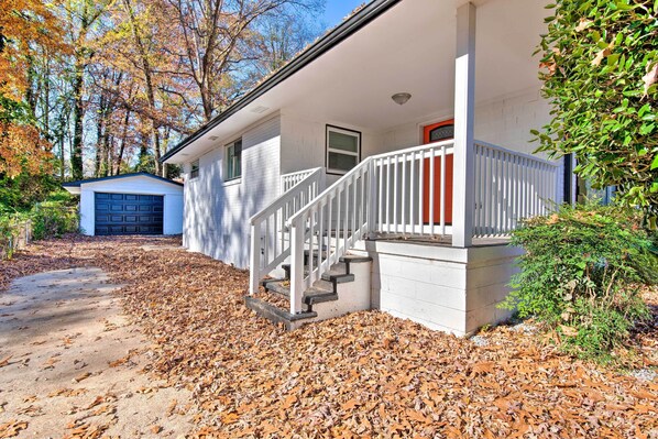 A two-story house with a front porch, a garage, and a driveway covered with fallen leaves.