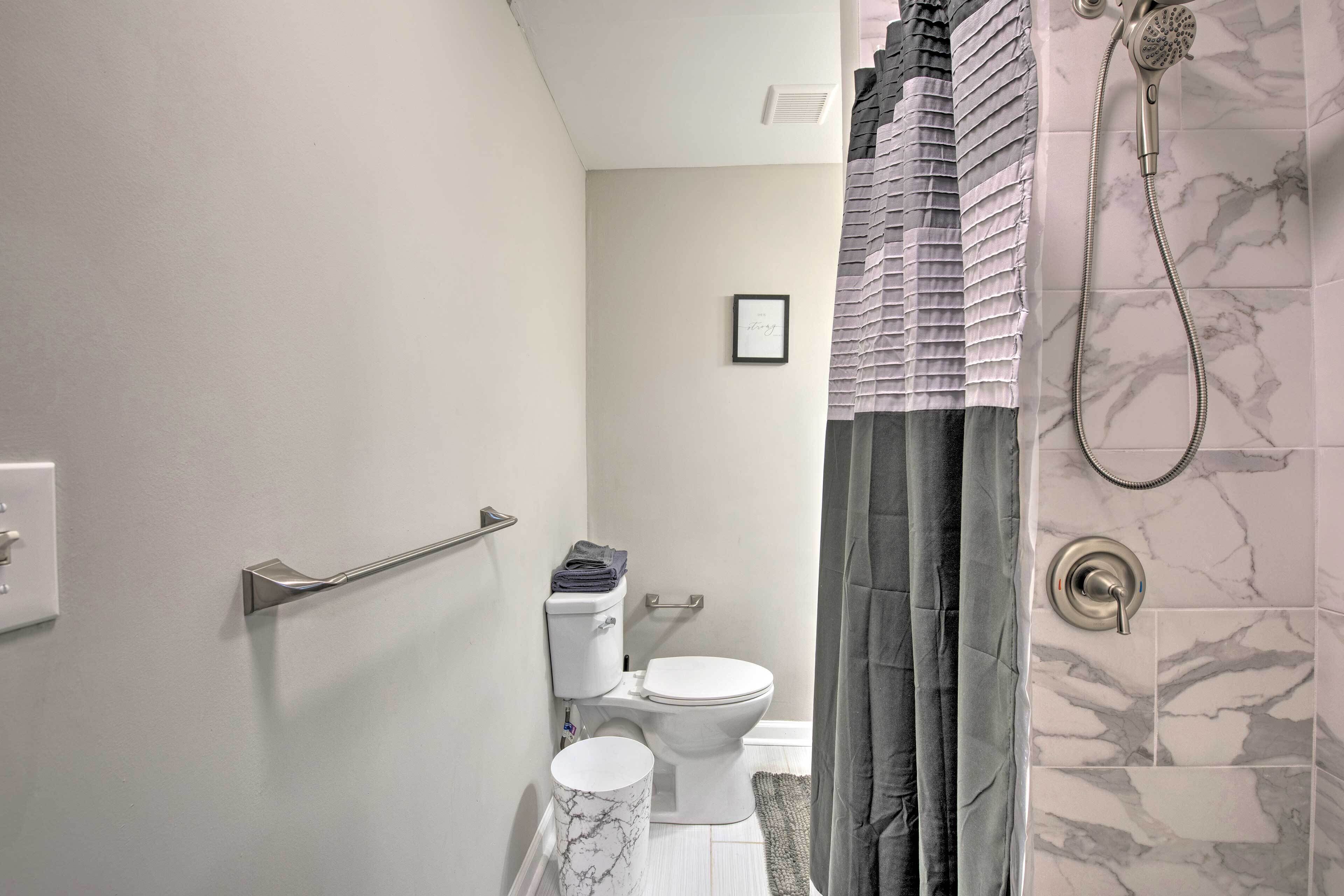 Une salle de bain comprenant des toilettes, un bidet, une douche avec un pommeau de douche amovible et un mur décoré d’un motif imitant le marbre.