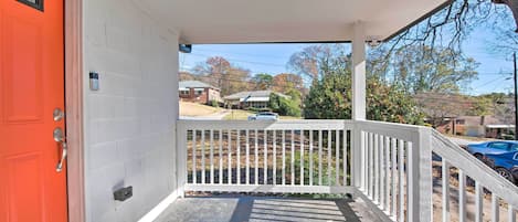 A porch with a white railing, a red door, and a view of a residential street.