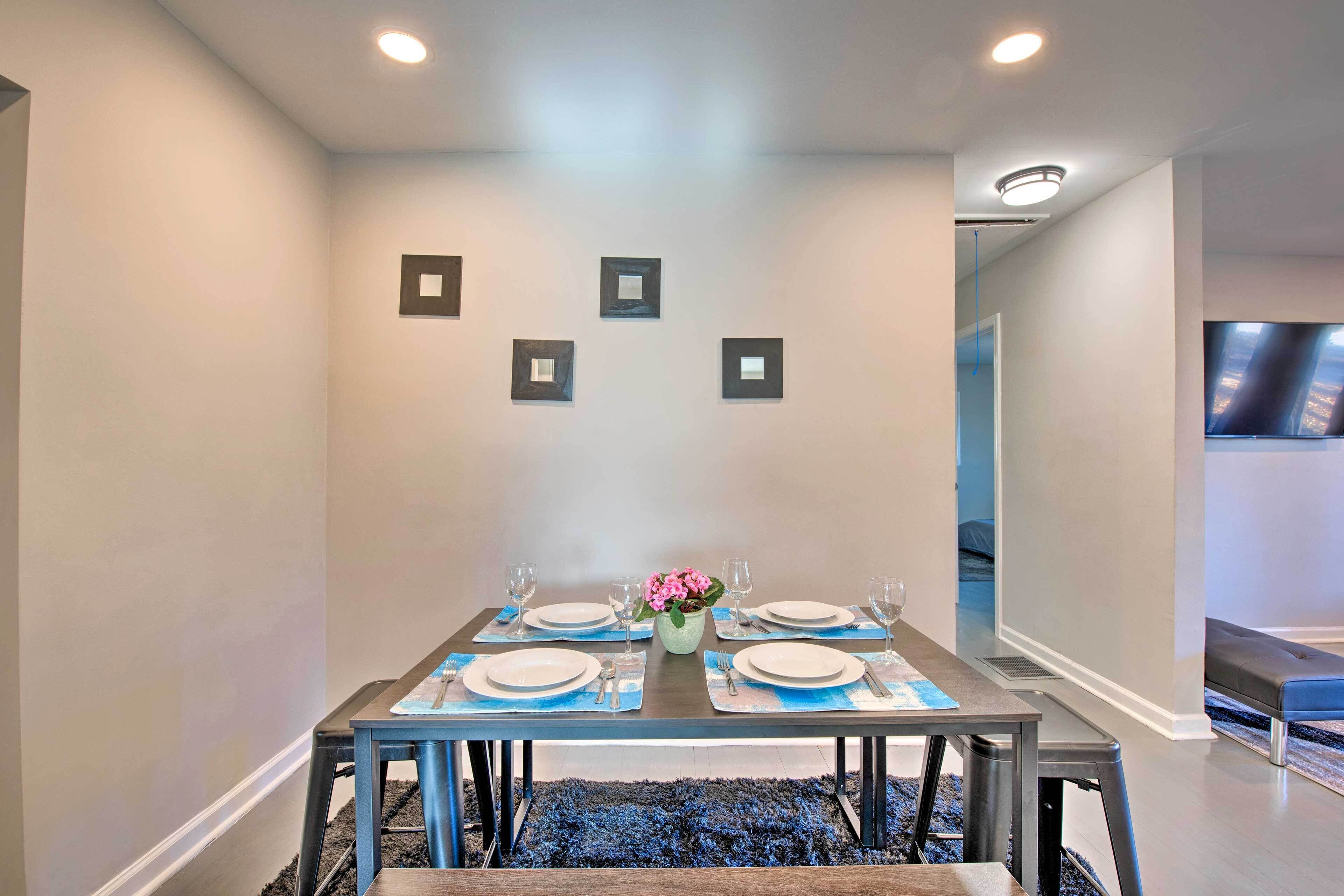A dining area with a table set for four, framed pictures on the wall, and a small vase with flowers.