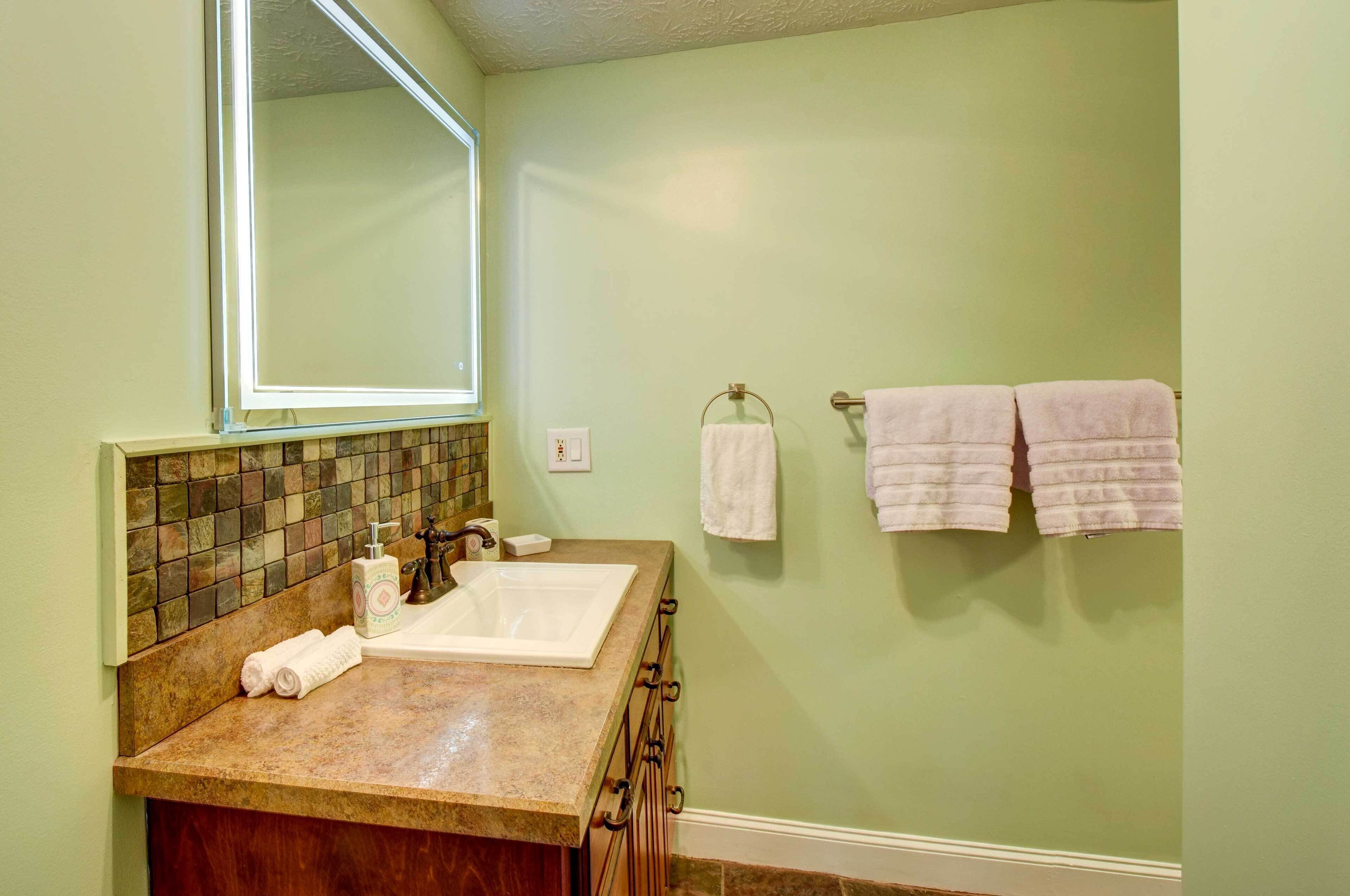 Un baño con un espejo grande, un lavabo y dos toallas colgadas en un perchero.