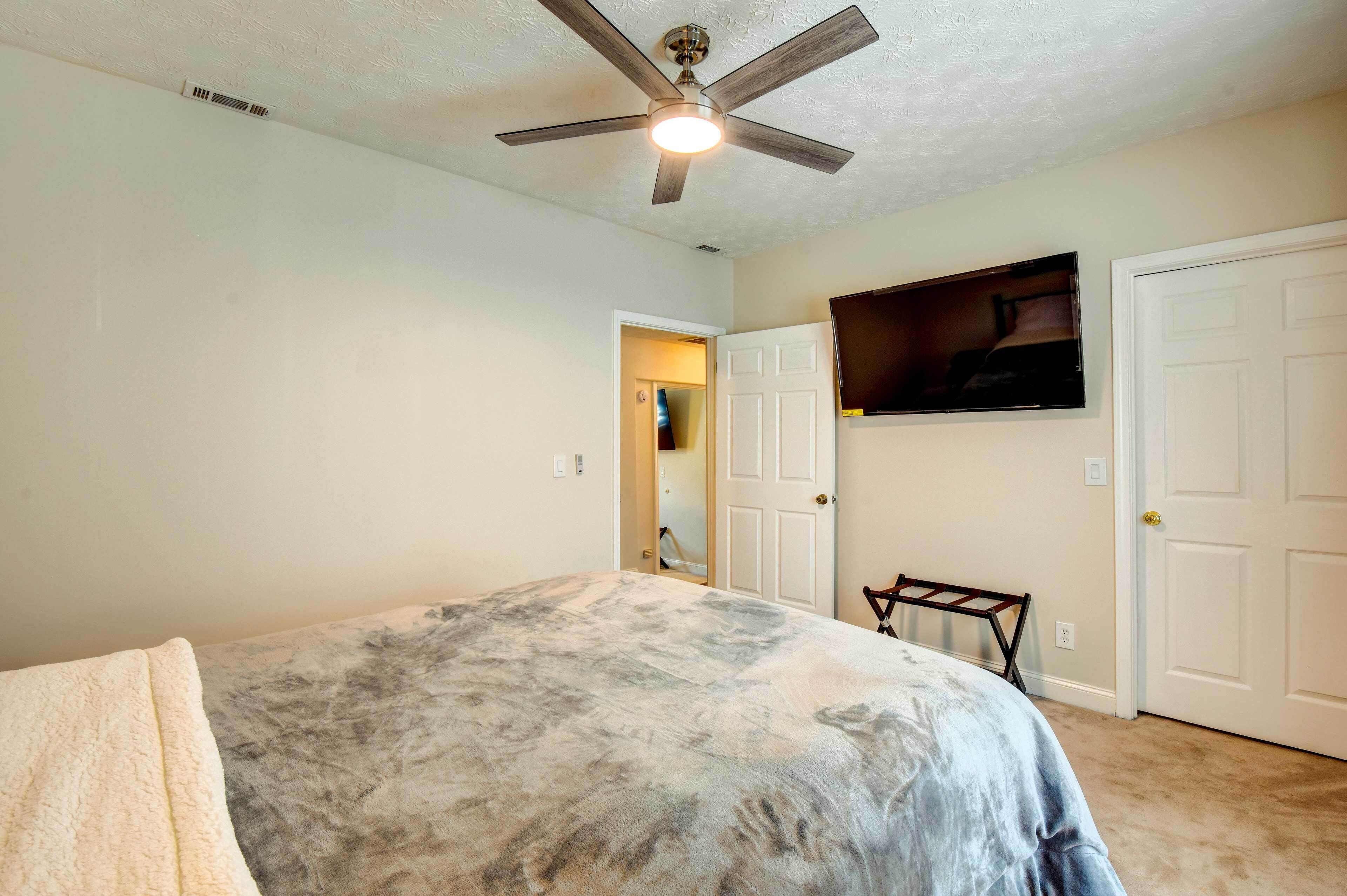 A bedroom with a bed, a ceiling fan, a TV mounted on the wall, and a door.