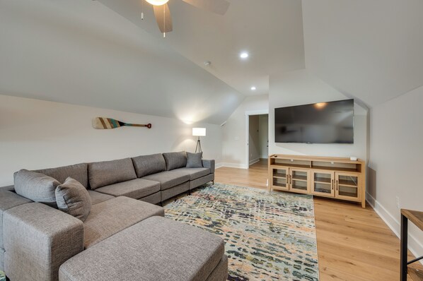 A modern living room with a sectional sofa, a patterned rug, and a TV on a wooden cabinet. - Spacious Lake Sinclair Vacation Rental w/ Dock! (Milledgeville)