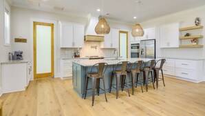 A modern kitchen with a central island, bar stools, white cabinetry, and pendant lighting.