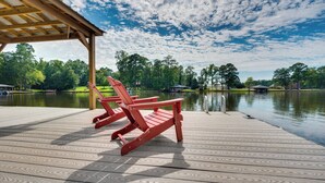A wooden deck with red Adirondack chairs overlooking a calm lake, surrounded by trees and a gazebo.