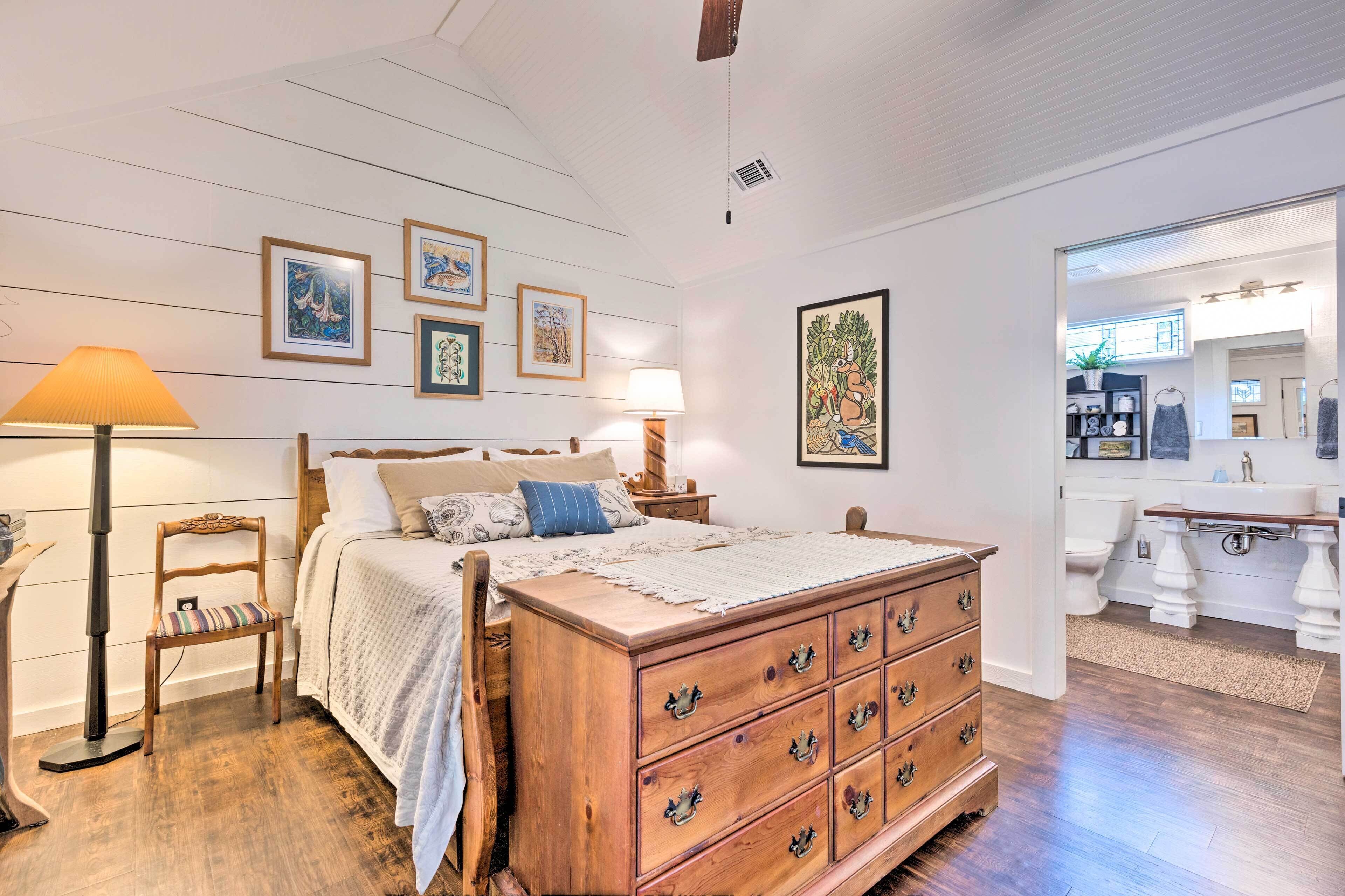 A bedroom with a wooden dresser, a bed with a white comforter, and a nightstand with a lamp.