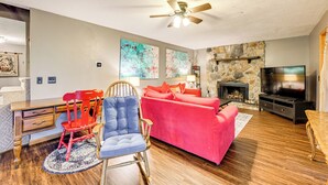 A living room with a stone fireplace, a television, a red sofa, a blue chair, and a wooden desk with drawers.