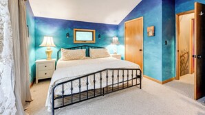 A bedroom with a bed, nightstands, a wooden door, and a window.