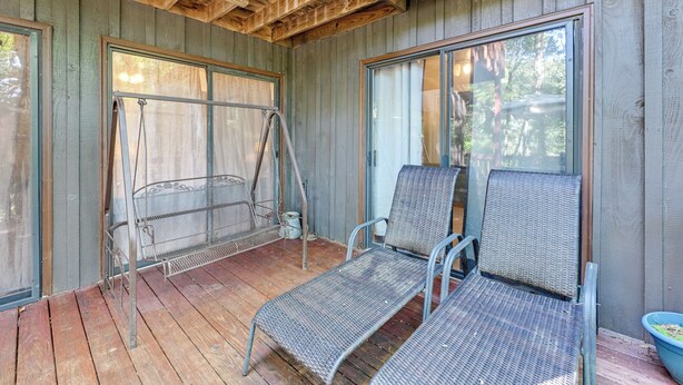 A covered porch with metal chairs and a metal bench, wooden flooring, and large windows.