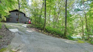 A rustic cabin with a gravel driveway, surrounded by dense forest.