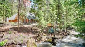 Una cabaña con fachada de madera, un porche y vistas a un río sinuoso rodeado de bosque denso.