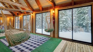 Una habitación acogedora con un ventanal grande, una hamaca colgante y una alfombra a cuadros.