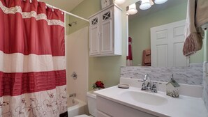 A bathroom with a shower curtain, a toilet, a sink with a mirror, and a cabinet. - Enchanted Forest Cottage w/ Hot Tub! (Hiawassee)