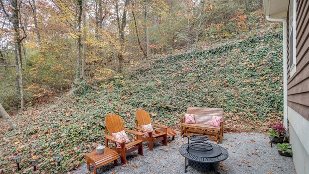 A patio with wooden furniture, including chairs and a bench, surrounded by a gravel area and a hillside covered in foliage. - Enchanted Forest Cottage w/ Hot Tub! (Hiawassee)