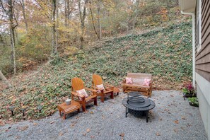 Eine Terrasse mit Holzmöbeln, darunter Stühle und eine Bank, umgeben von einem Kiesbereich und einem mit Vegetation bewachsenen Hügel.