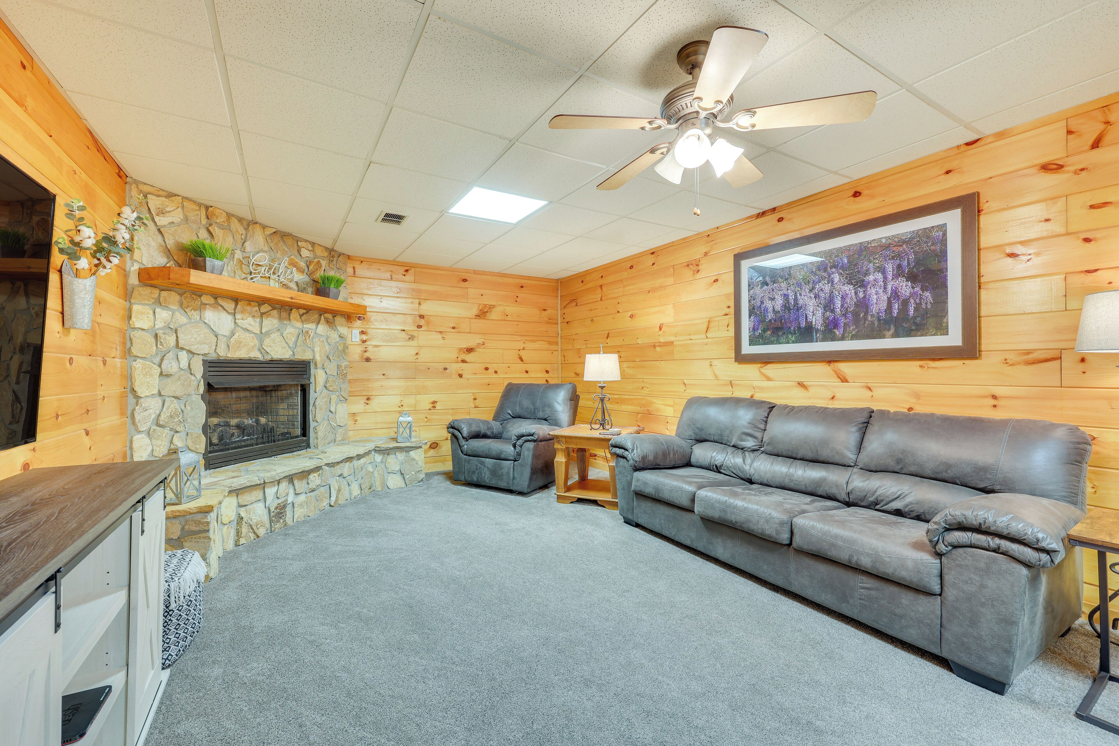 A cozy living room with a stone fireplace, leather sofas, and a ceiling fan.