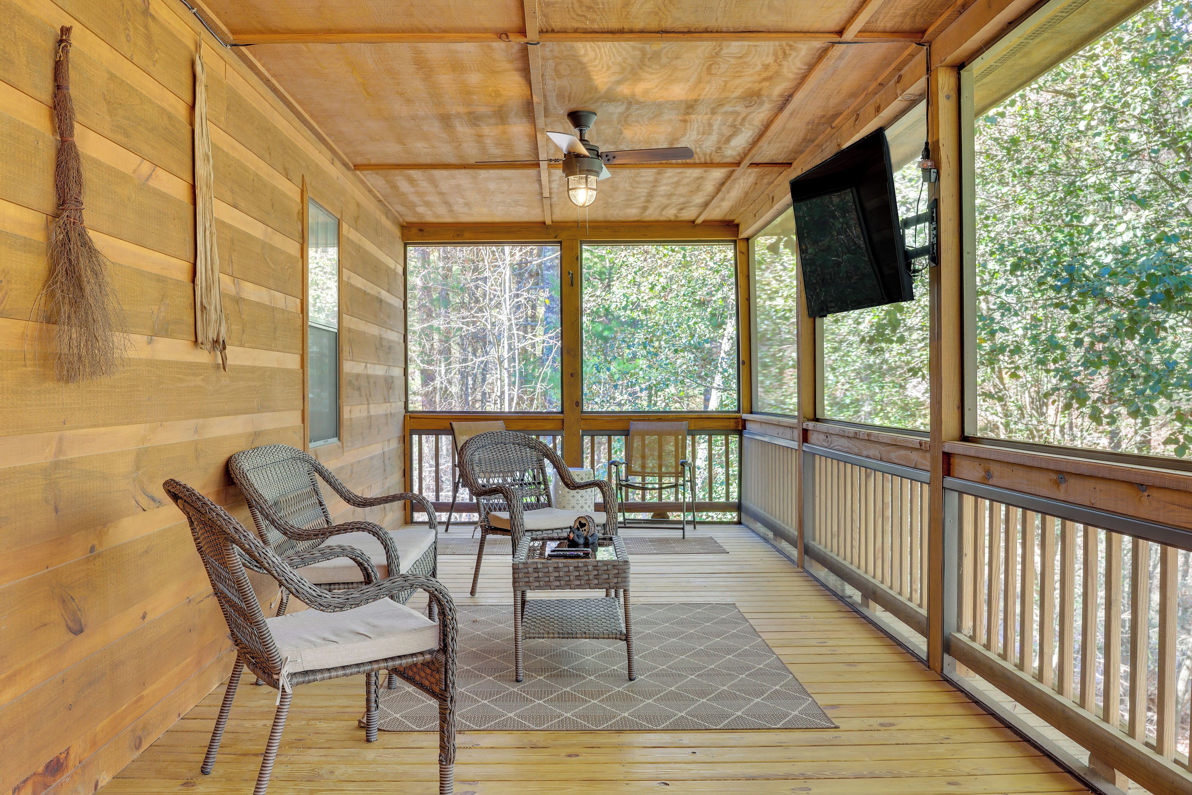 A wooden deck with wicker furniture, a ceiling fan, and a mounted TV.