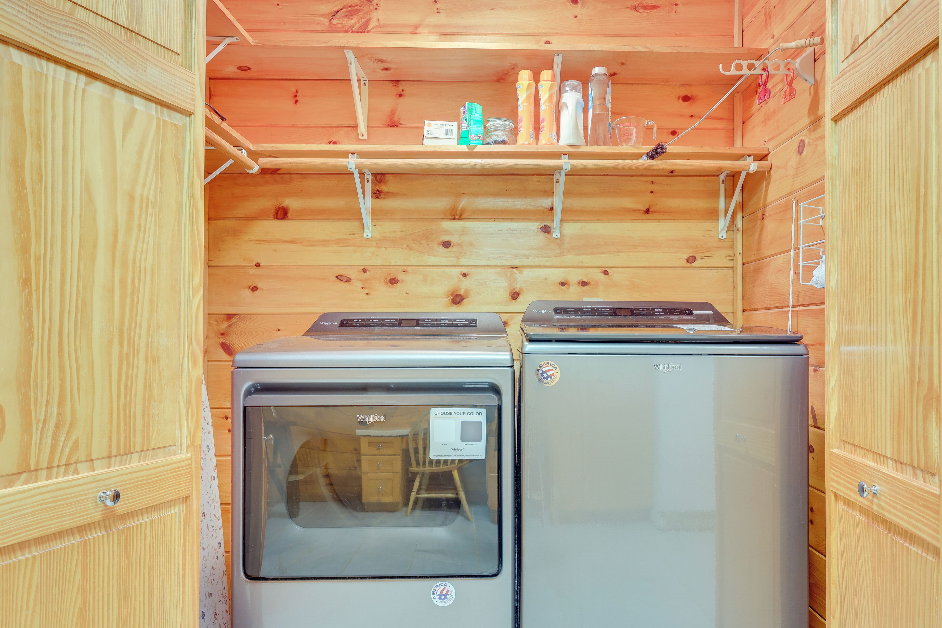 Un espace cuisine compact comprenant deux réfrigérateurs, une étagère en bois avec divers objets, et une fenêtre avec une chaise à l’intérieur.