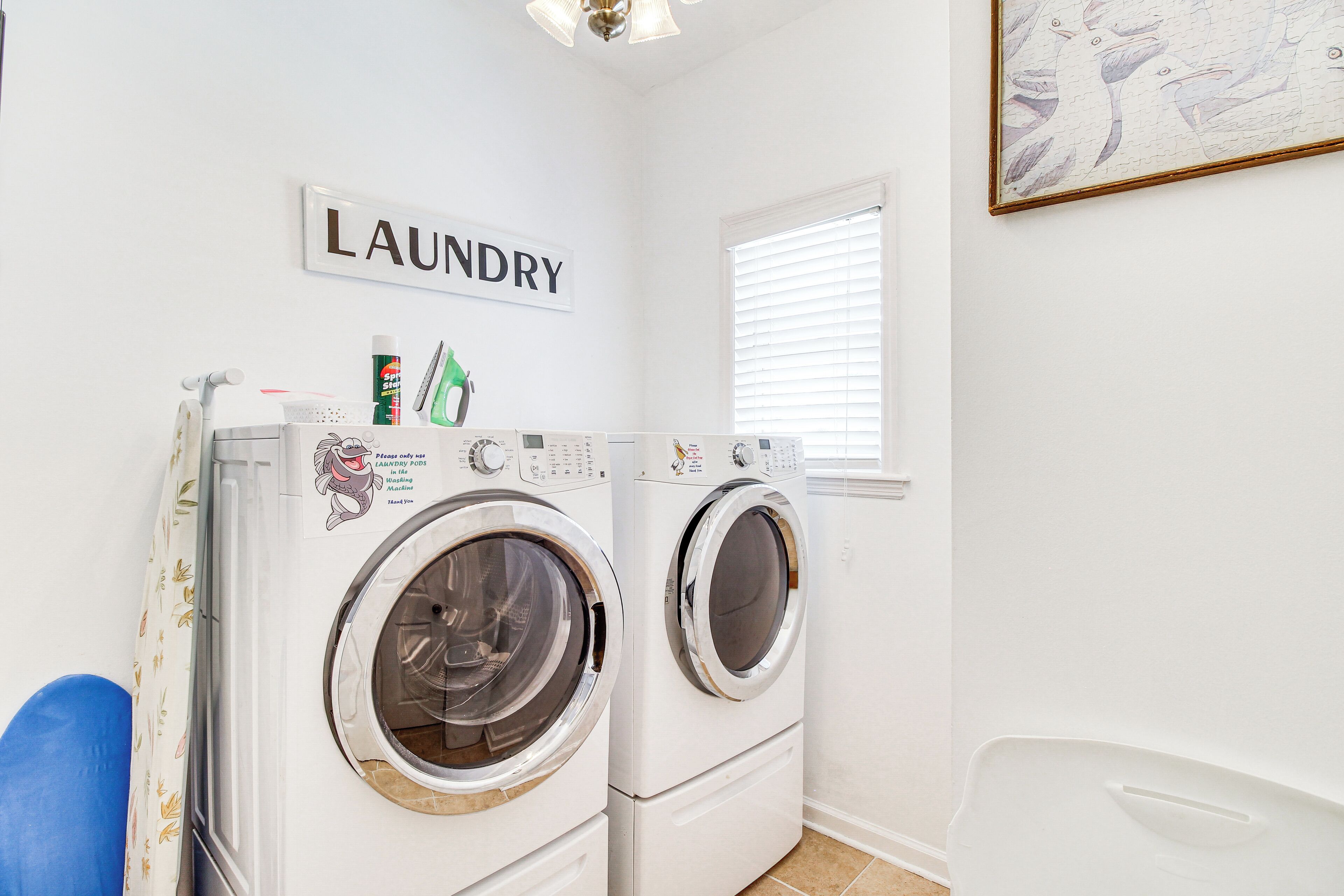 A laundry room with two stacked front-loading washing machines, a wall-mounted sign labeled "LAUNDRY", and a window with blinds.