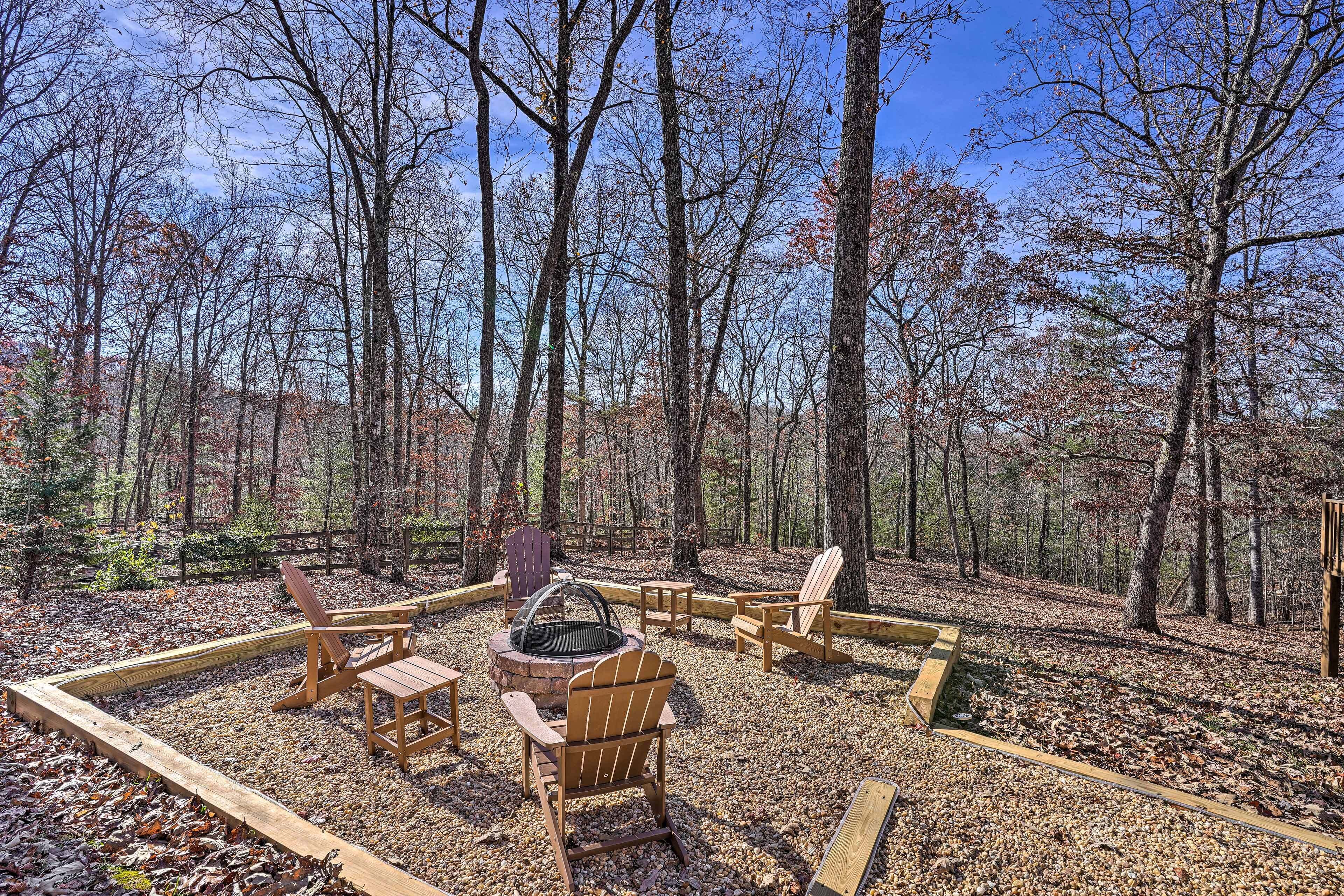 An outdoor seating area with Adirondack chairs and a fire pit surrounded by a wooden deck in a forested setting.