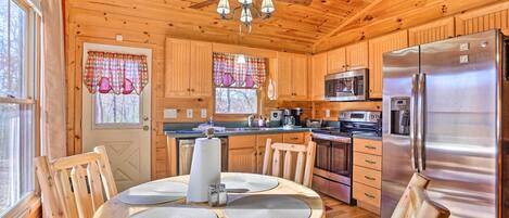Une cuisine rustique aménagée dans une cabane en bois, avec une table à manger, des chaises, un réfrigérateur, un four à micro-ondes et un ventilateur de plafond.