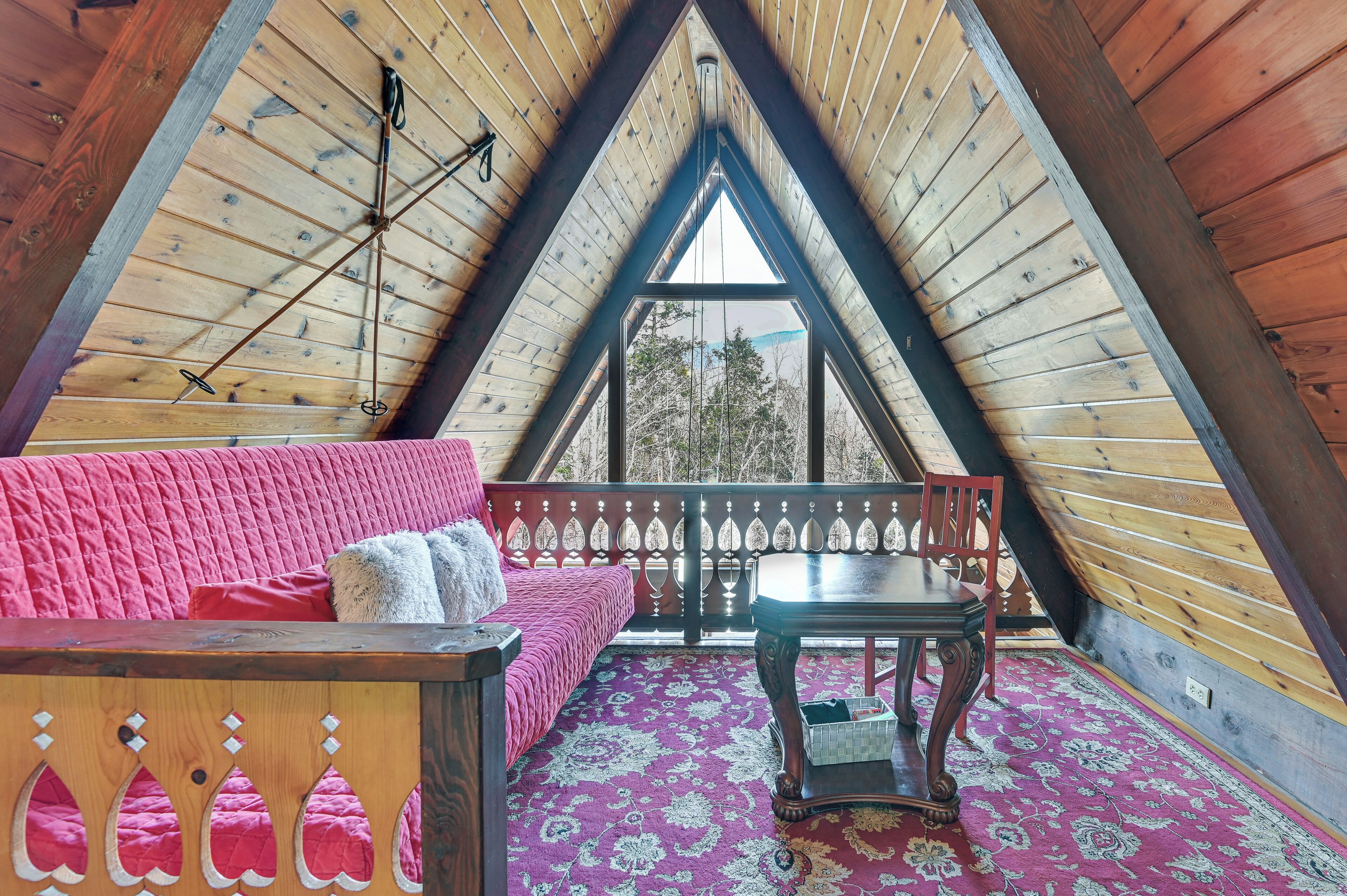 Una habitación acogedora en el ático, con techo inclinado, un sofá rosa, una mesa de madera y una alfombra estampada.