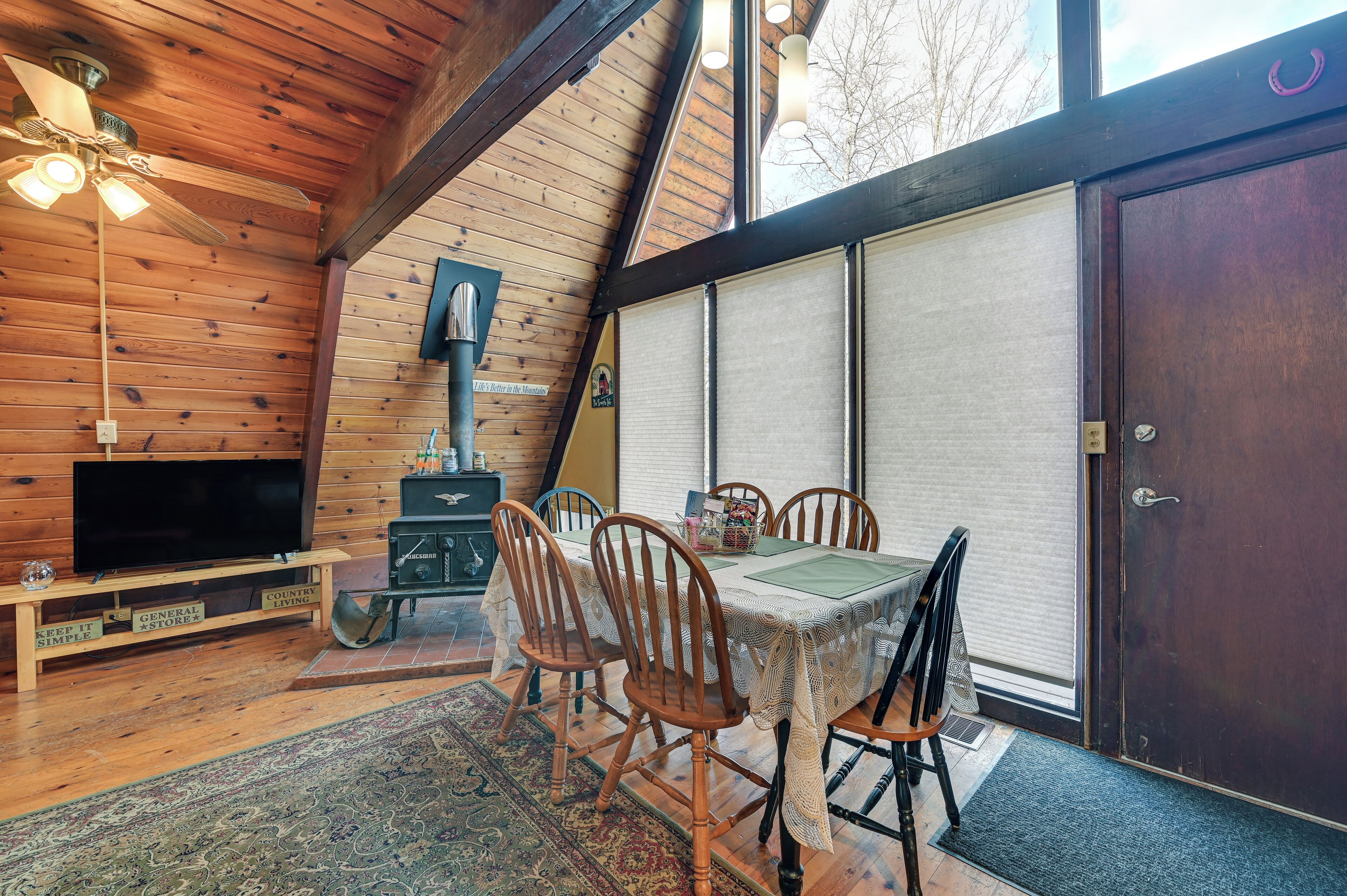 A cozy wooden cabin interior with a dining table, chairs, a television, and a fireplace.