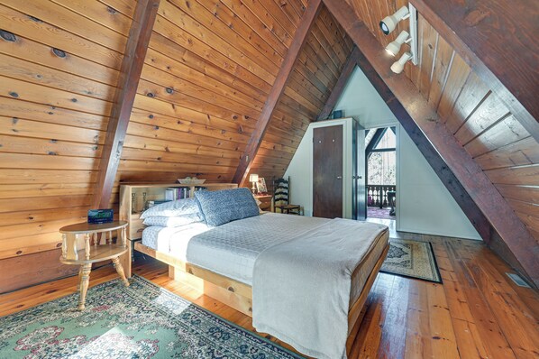 A cozy attic bedroom with a wooden sloped ceiling, a bed with a white comforter, and a small wooden nightstand.