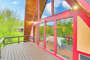 A wooden deck with a glass enclosure, a red exterior, and a view of a patio with tables and chairs.