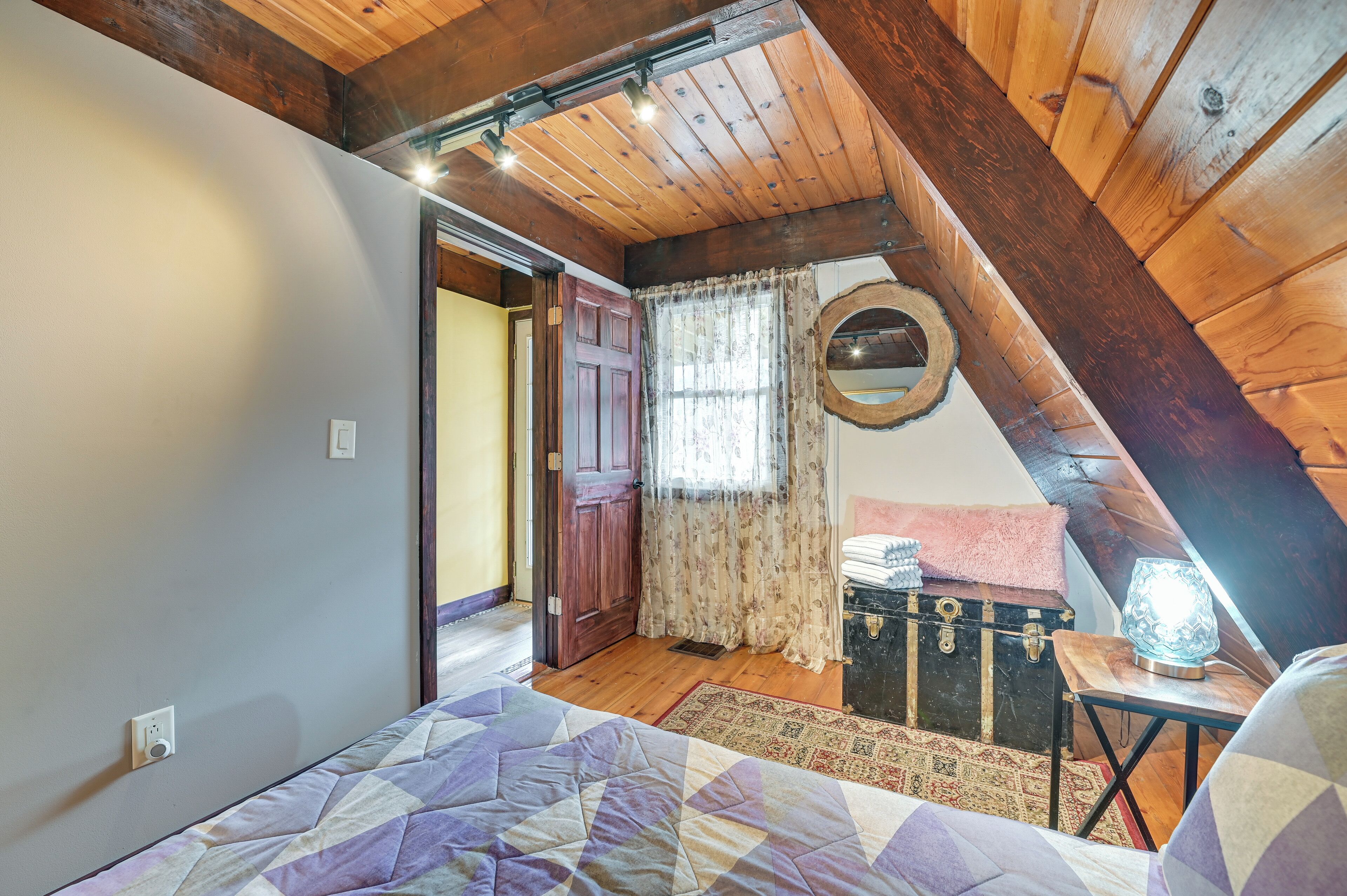 A bedroom with a sloped ceiling, a wooden door, a vintage suitcase, and a quilted bedspread.