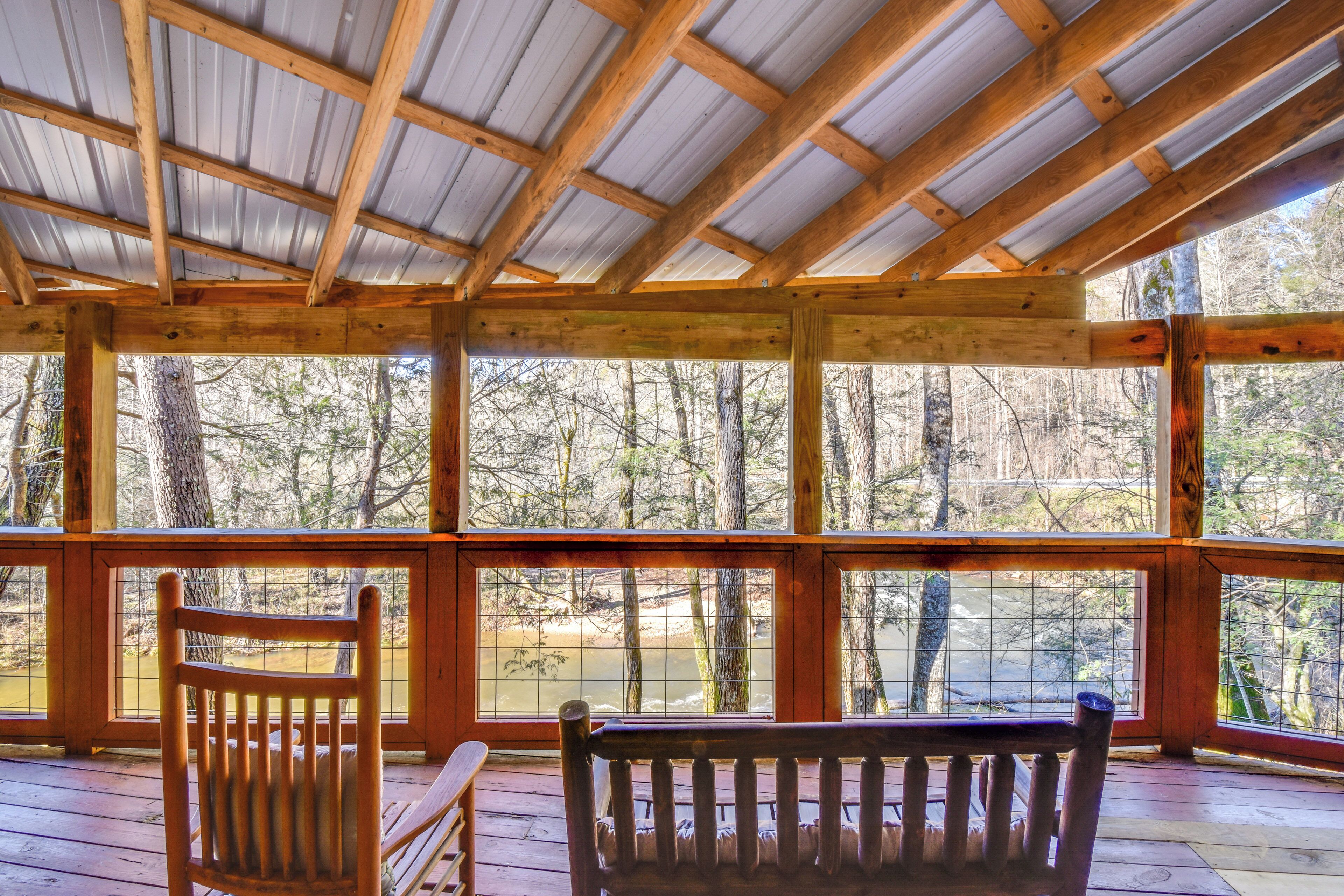 A wooden deck with a metal roof, wooden benches, and a view of a forest.