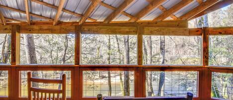 A wooden deck with a metal roof, wooden benches, and a view of a forest.