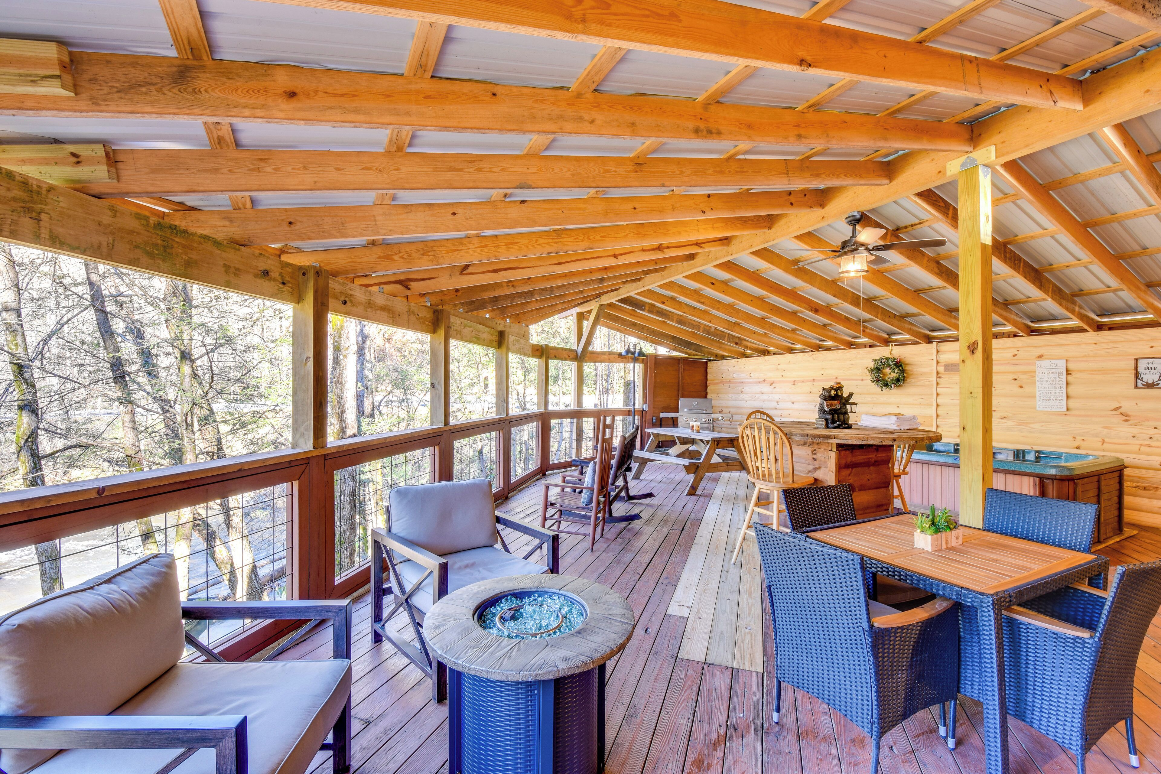 A wooden deck with outdoor furniture, a fire pit, and a view of the surrounding forest.