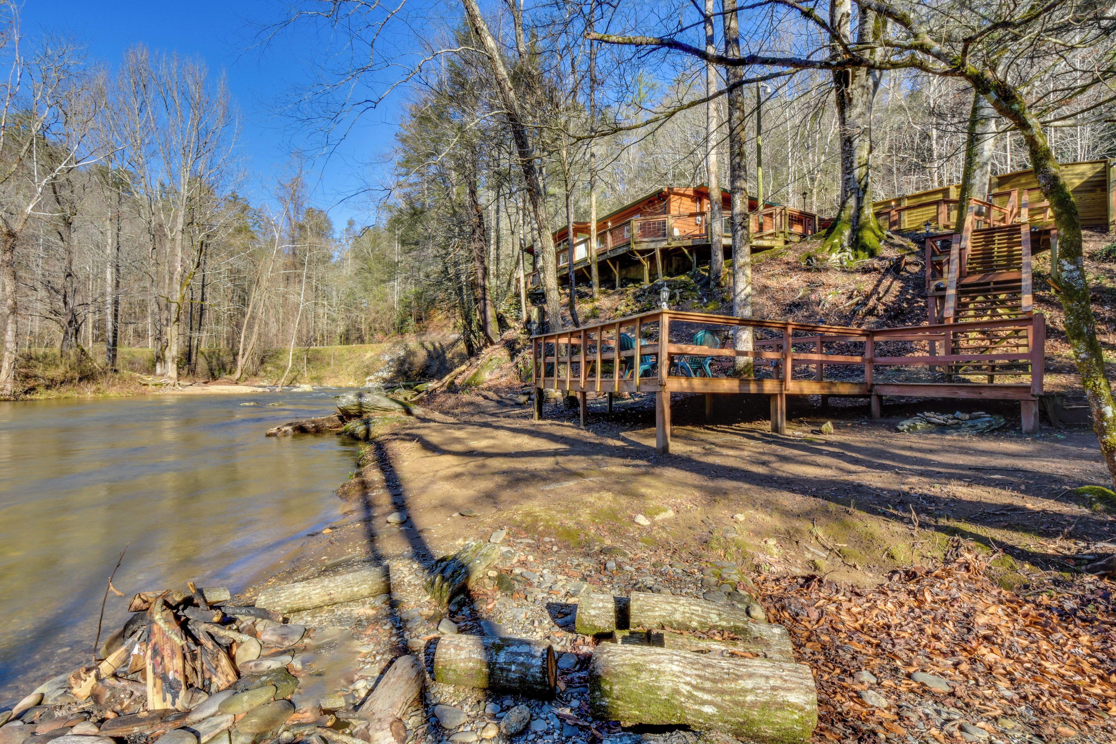 Une cabane dotée d’une terrasse donnant sur une rivière, entourée d’arbres.