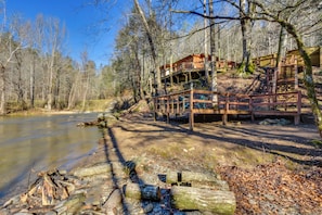 Eine Holzhütte mit einer Terrasse, die auf einen Fluss mit Blick auf Bäume blickt.
