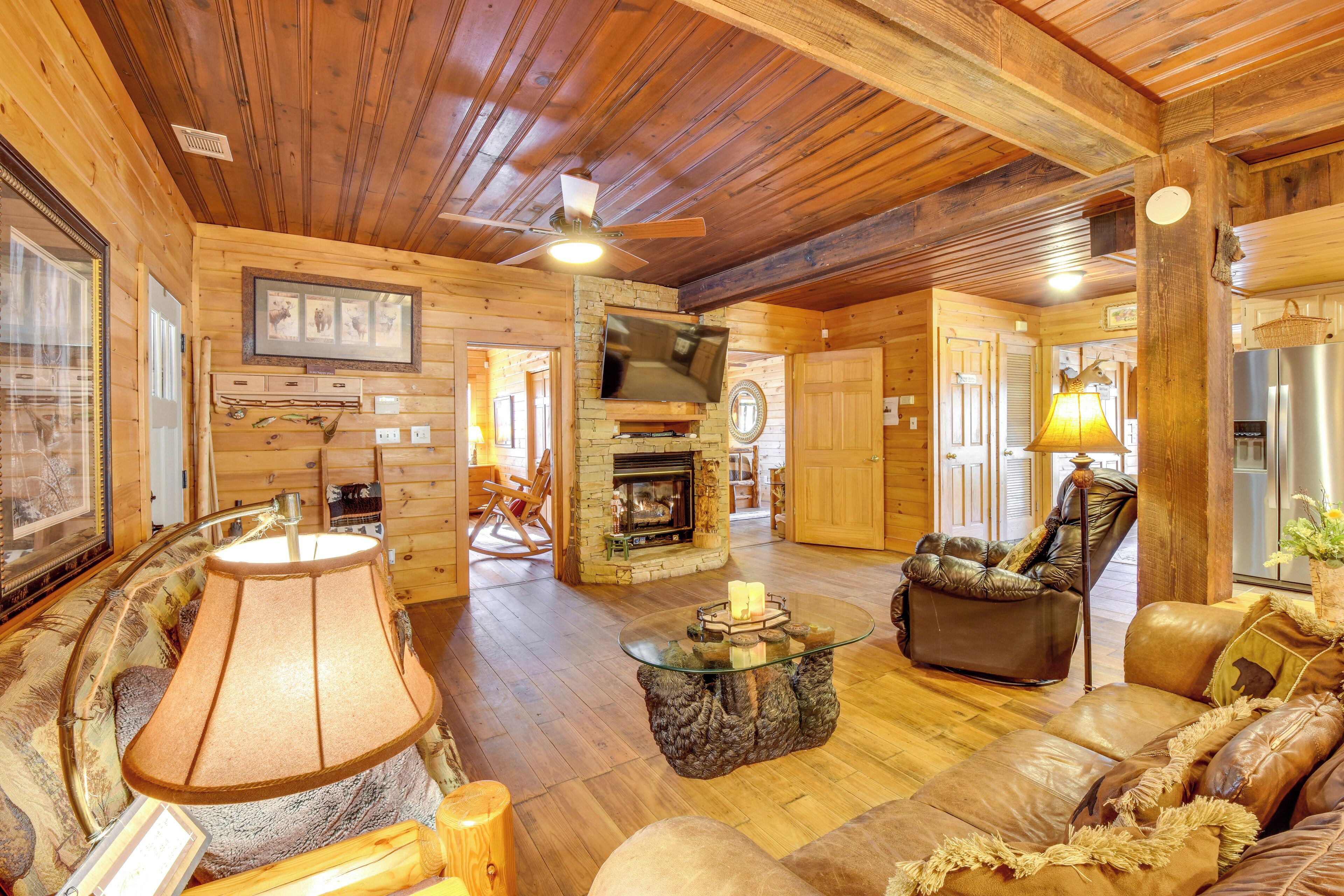 A cozy log cabin interior with a fireplace, leather furniture, and a stone accent wall.