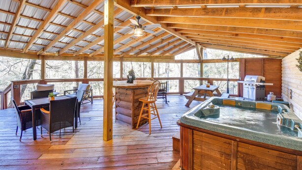 A wooden deck with a hot tub, outdoor seating, and a grill area. - Riverfront Helen Cabin w/ Hot Tub & Deck! (Helen)