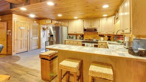 A spacious kitchen with wooden cabinets, a central island with stools, stainless steel appliances, and a sign detailing hot tub rules. - Riverfront Helen Cabin w/ Hot Tub & Deck! (Helen)