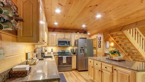 Une cuisine de style rustique, avec des murs en bois, des comptoirs en granit, des appareils électroménagers en acier inoxydable et un escalier en bois.
