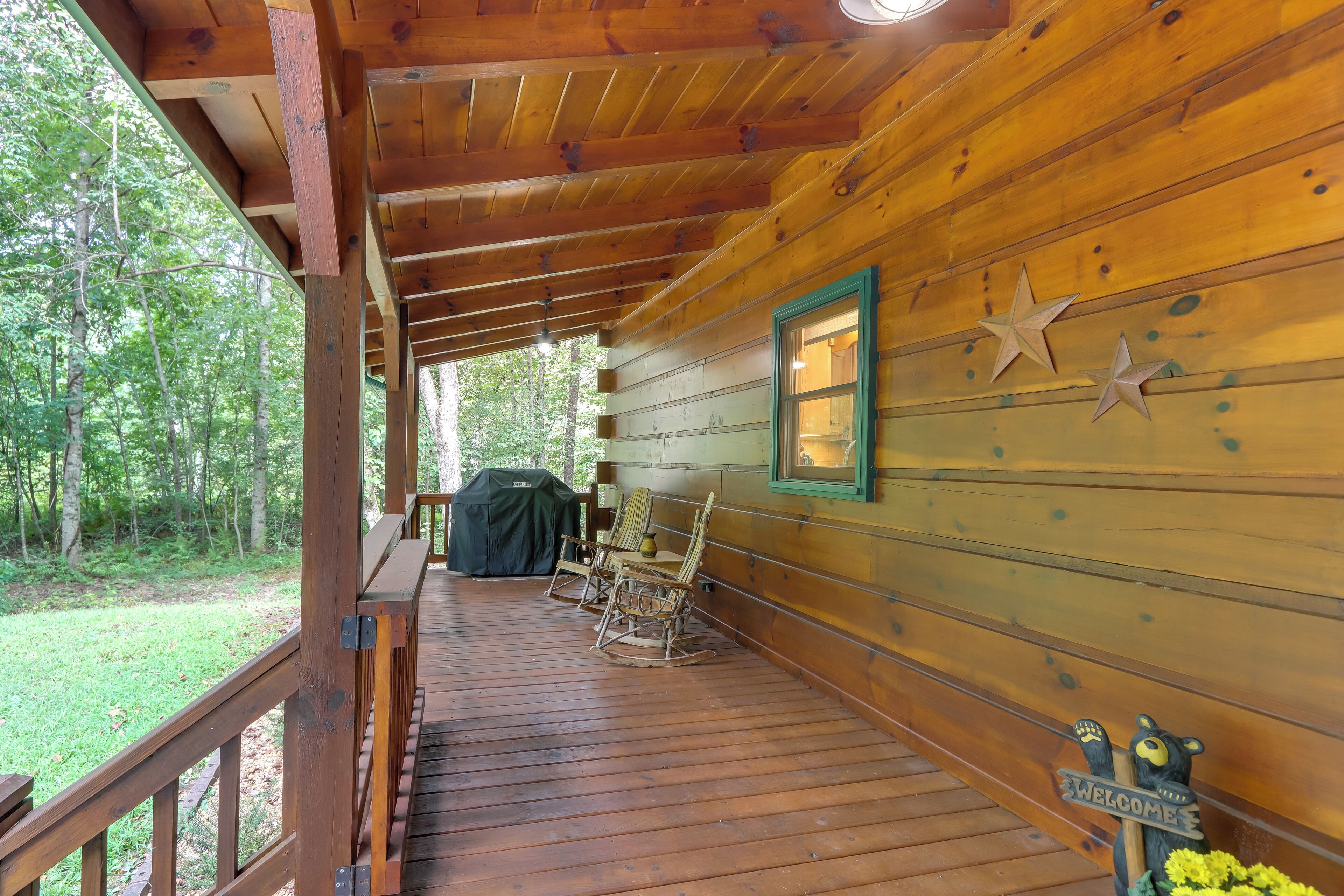 A wooden cabin with a porch, rocking chairs, a grill, and a welcome sign.