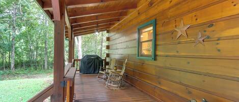 A wooden cabin with a porch, rocking chairs, a grill, and a welcome sign.