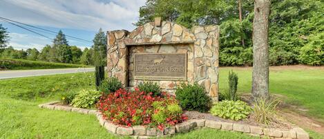 A stone sign with a deer logo and text for 'Little Sugar Creek Estates' in a landscaped area with grass and plants.