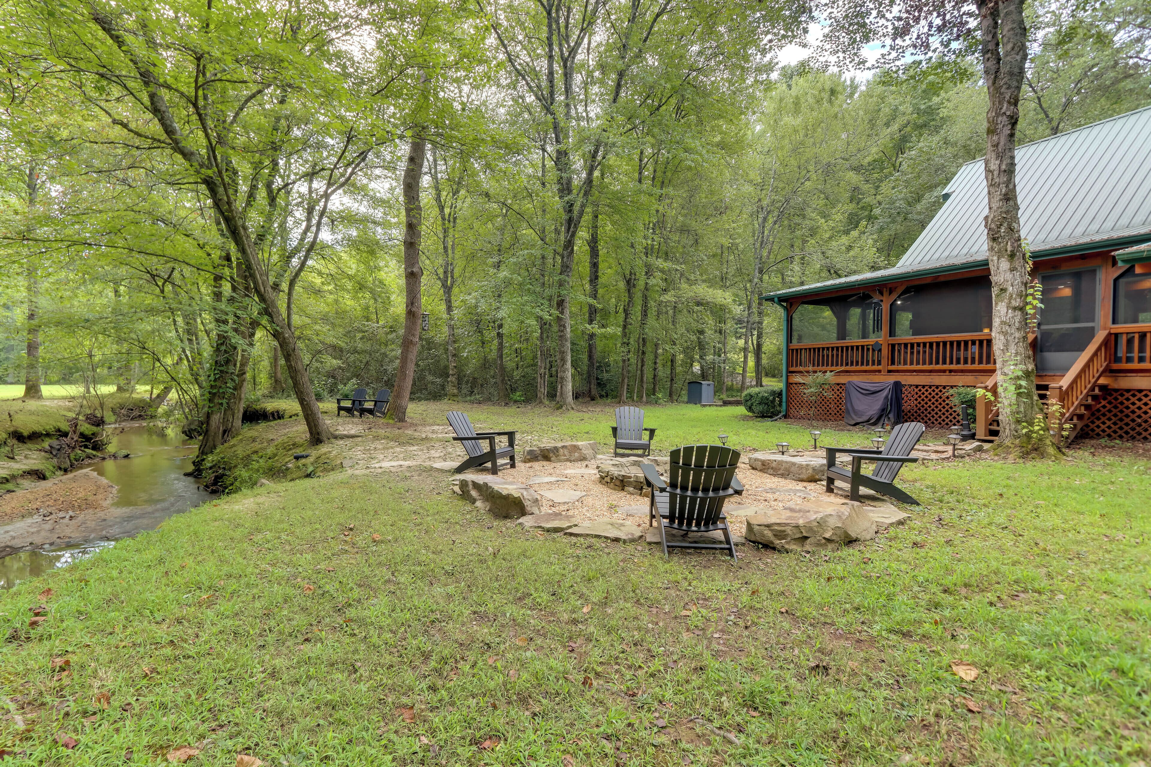 A cabin with a deck, a fire pit, and chairs in a wooded area.