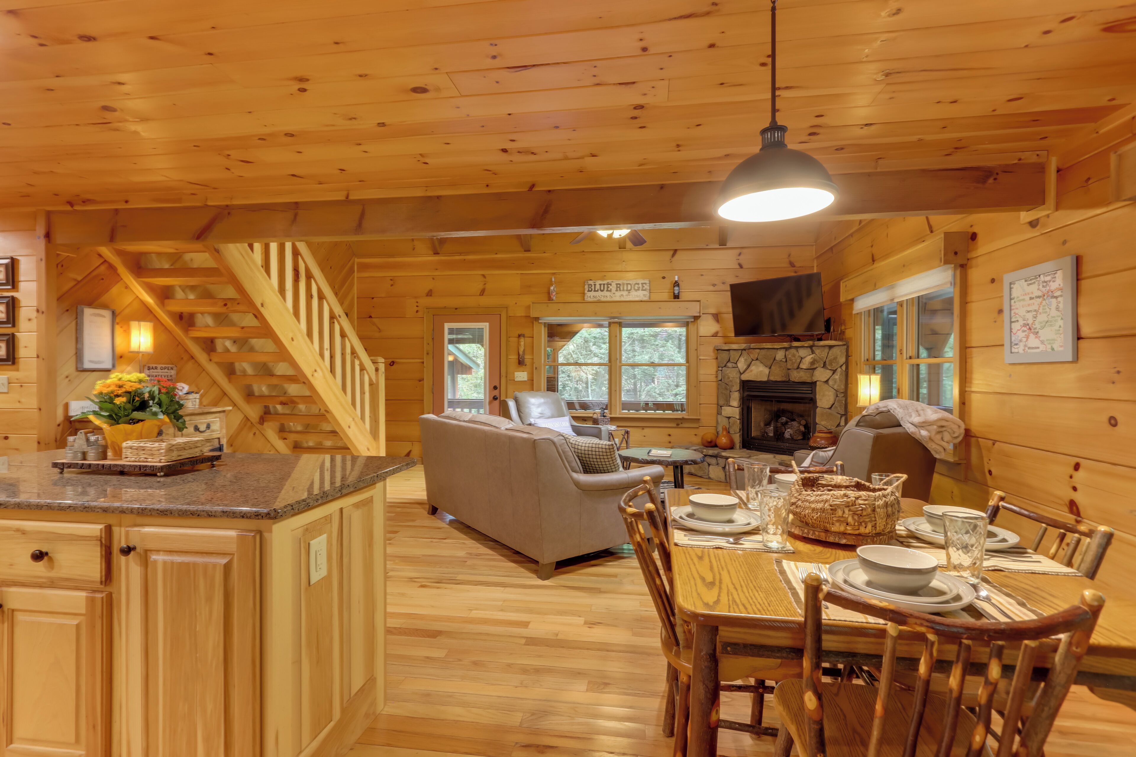 Interior acogedor de una cabaña con comedor, sofá, chimenea y escalera.