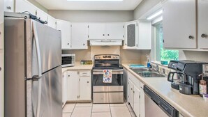 Una cocina compacta con armarios blancos, un refrigerador de acero inoxidable, un horno, un lavavajillas y una cafetera.